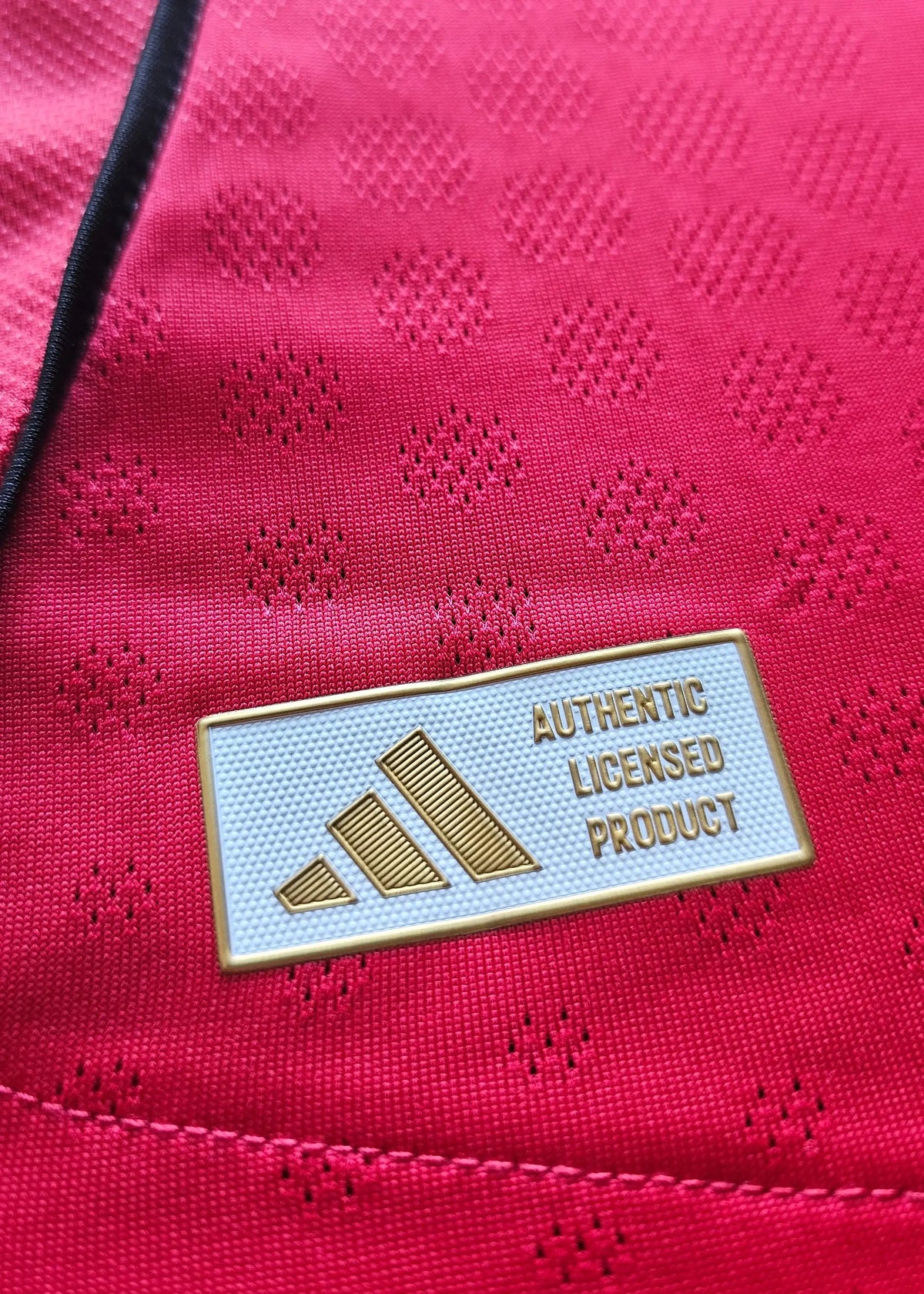Close-up of the gold adidas Authentic Licensed Product tag stitched into Bendito Mantato's red Manchester United F.C. shirt, No. 70, 2025-2026.