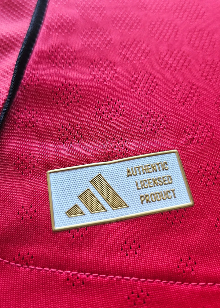 Close-up of the gold adidas Authentic Licensed Product tag stitched into Bendito Mantato's red Manchester United F.C. shirt, No. 70, 2025-2026.