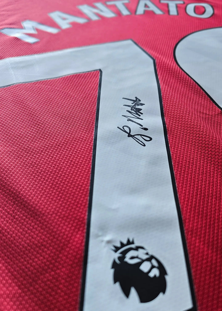 Close-up of the white No. 70 with a black-ink autograph and the Premier League crest patch beneath it, on Bendito Mantato's red Manchester United shirt.