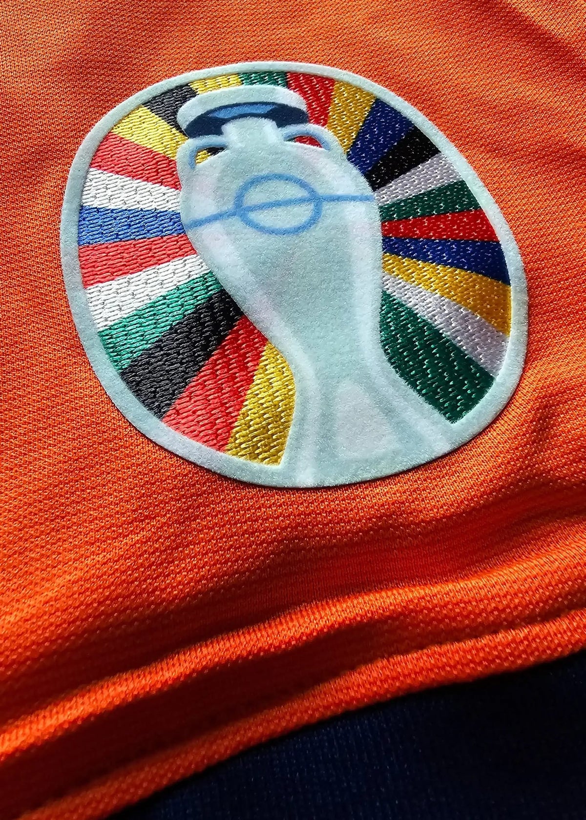 Embroidered patch with a stylized face in sunglasses framed by sunburst rays, on Brian Brobbey's orange Holland shirt, No. 19.