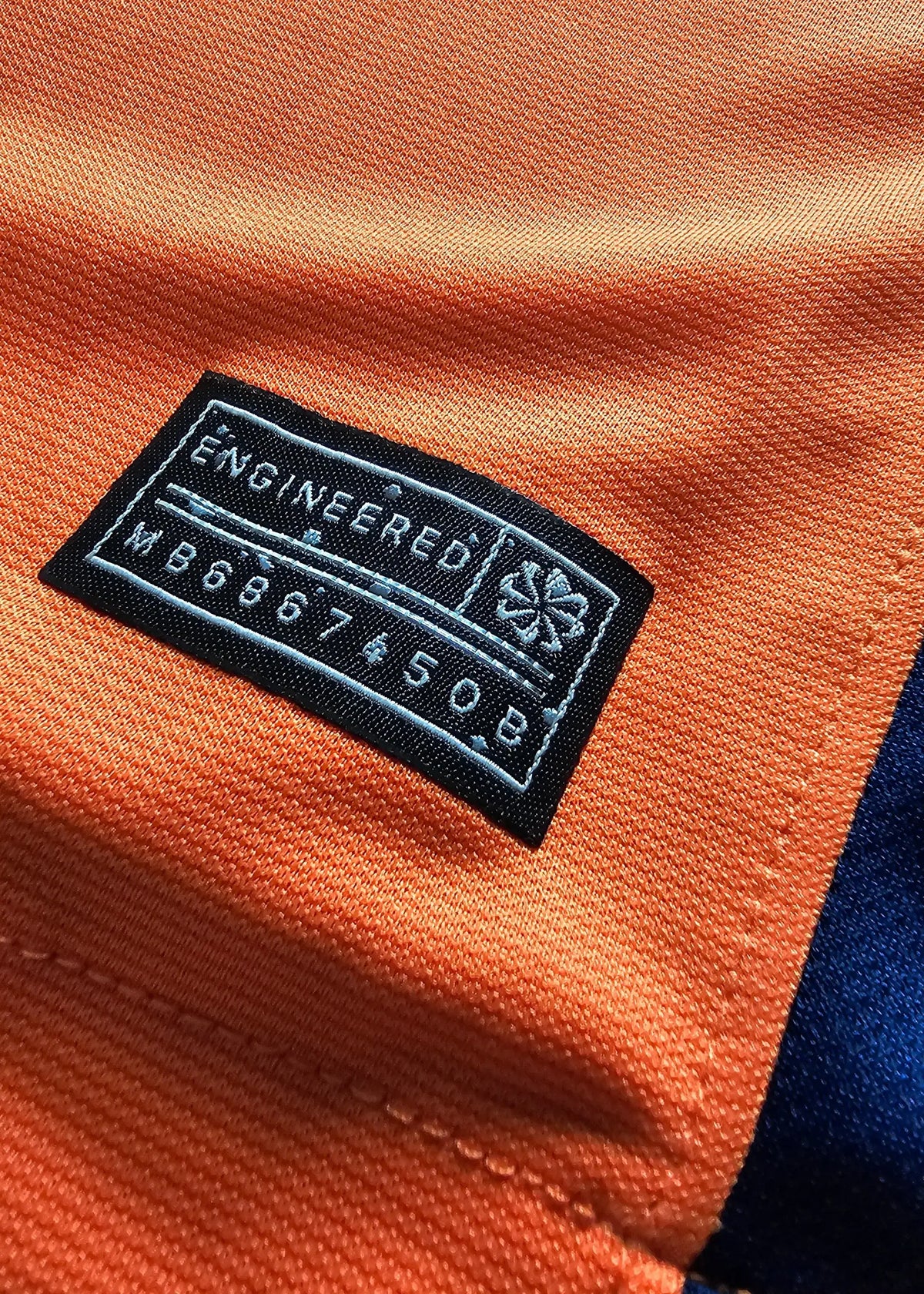 Close-up of an inner 'Engineered' size and care label stitched into the collar seam of Brian Brobbey's orange Holland shirt, No. 19.