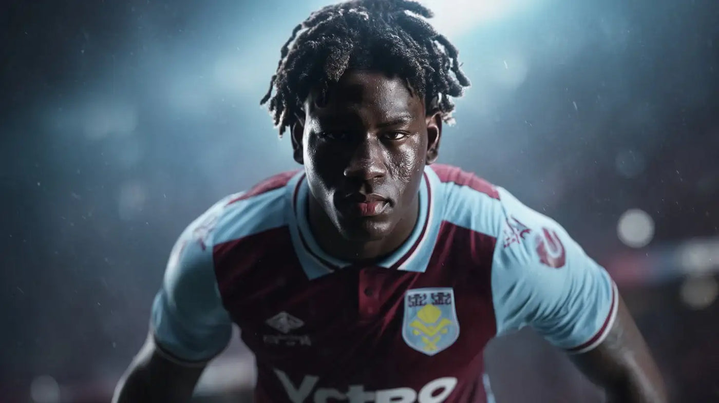Brian Madjo in Aston Villa claret and light blue football shirt, intense close-up in rainy stadium setting.