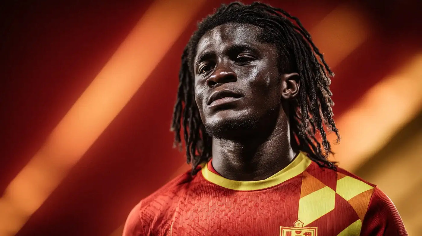 Caleb Yirenkyi in Nordsjaelland red football shirt with yellow and orange geometric pattern and club badge under stadium lighting.