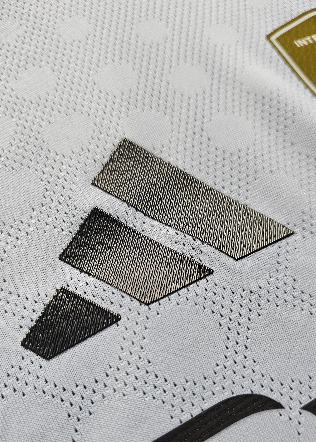 Close-up of the adidas three-stripe logo on the shoulder of the Real Madrid shirt, gold badge visible in the corner.