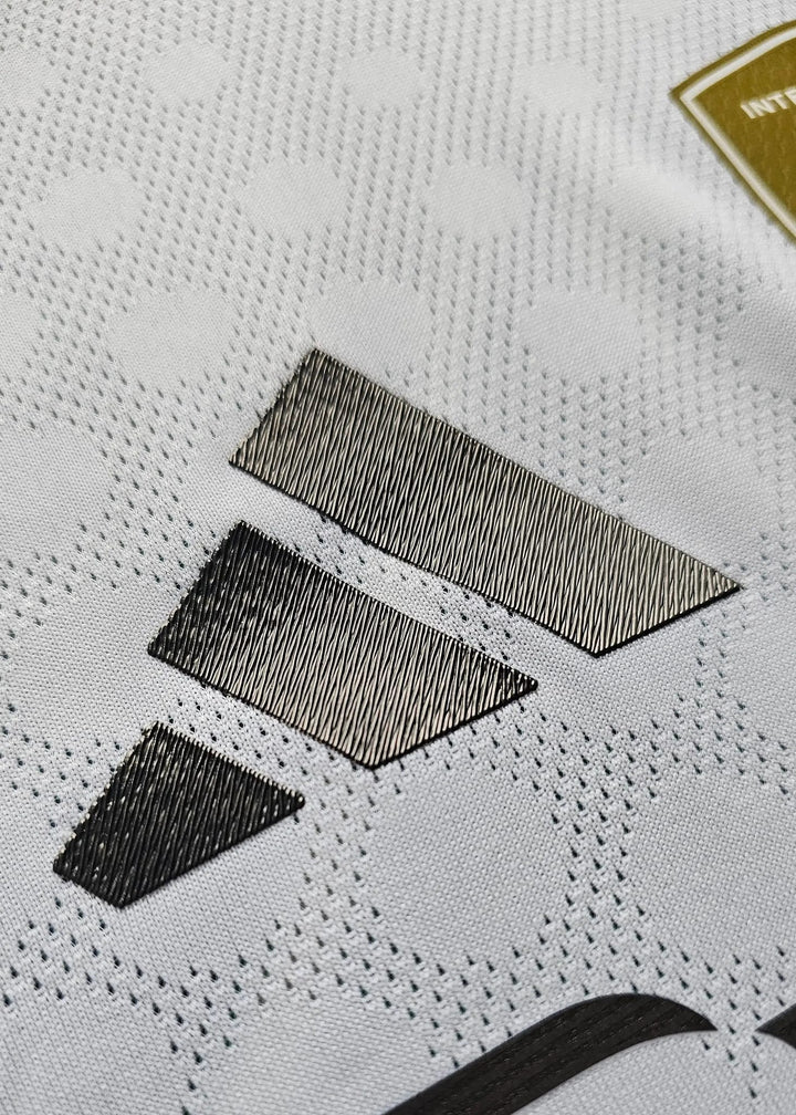 Close-up of the adidas three-stripe logo on the shoulder of the Real Madrid shirt, gold badge visible in the corner.