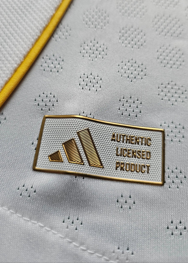 Close-up of the adidas Authentic Licensed Product tag near the hem, beside the yellow trim of the Real Madrid shirt.