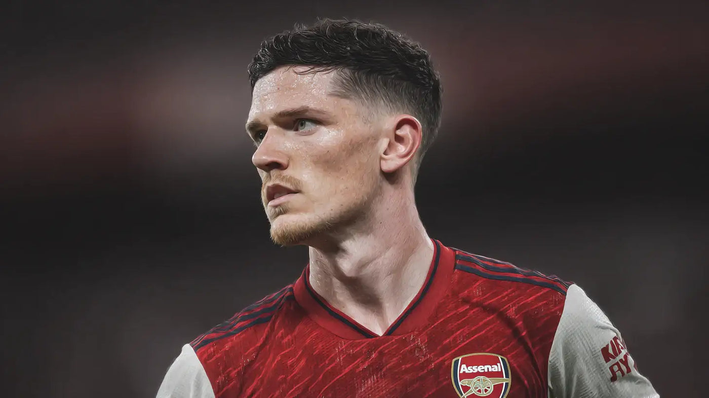 Declan Rice looking to the side in an Arsenal home football shirt, detailed close-up against a dark background.