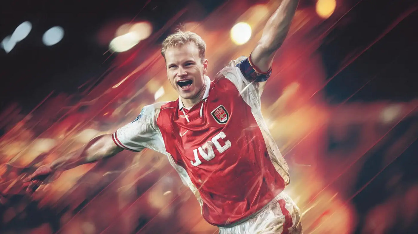 Dennis Bergkamp celebrates in an Arsenal kit, arms outstretched during a dramatic night match.
