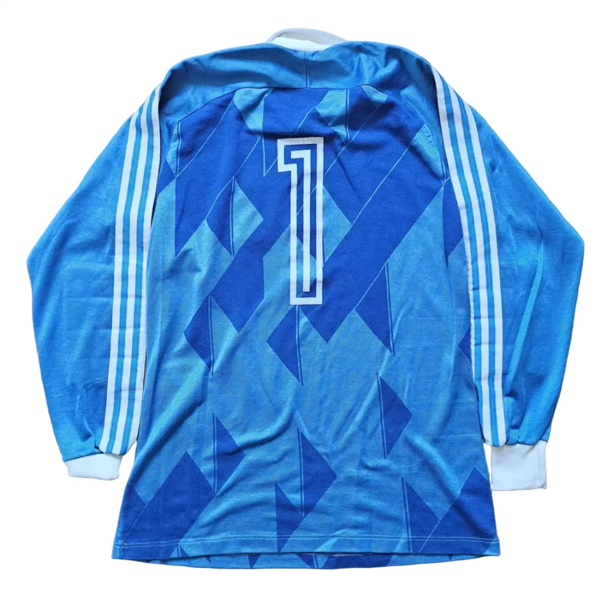 A blue long-sleeve soccer jersey with a geometric pattern, white number 1 on the back, and three white stripes on the sleeves, laid flat on a light wood floor.