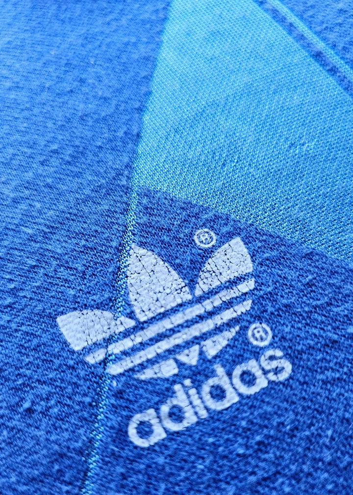 Embroidered adidas trefoil logo with the adidas wordmark, stitched onto the blue fabric of Eike Immel's West Germany 1987-88 shirt.
