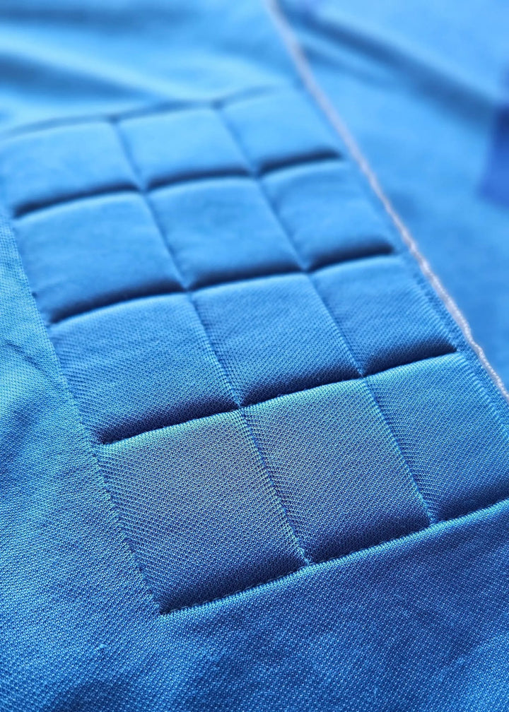 Close-up of a bright blue quilted fabric panel with stitched square pockets on a matching blue textile background.