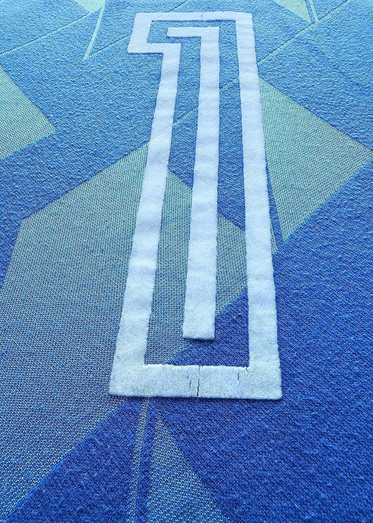 Close-up of a blue patterned fabric with a large white outlined number 1 printed or stitched onto it.