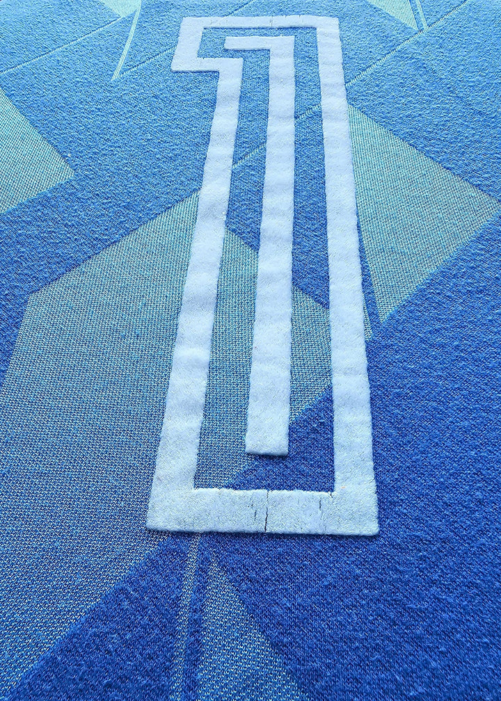 Close-up of a blue patterned fabric with a large white outlined number 1 printed or stitched onto it.