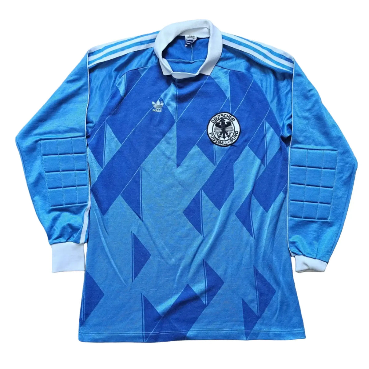 Front of a blue diamond-pattern goalkeeper shirt with padded elbows, an Adidas logo and a crest, Eike Immel's West Germany 1987-1988 No. 1 shirt.