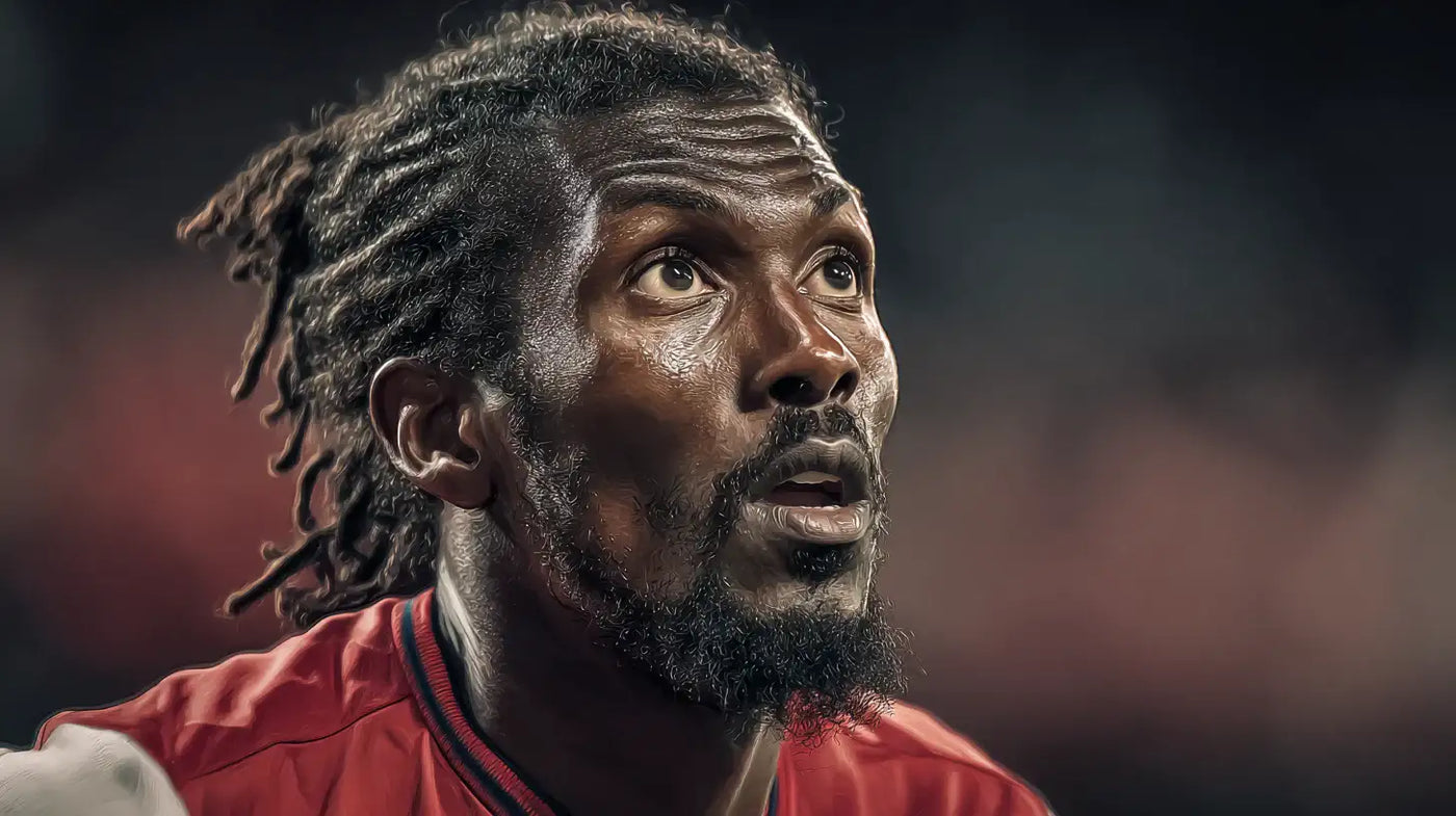 Emmanuel Adebayor gazing upward in an Arsenal football shirt, dramatic arena lighting and soft background bokeh.