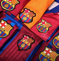 Close-up of FC Barcelona crests in red, blue, and orange on multiple soccer jerseys.