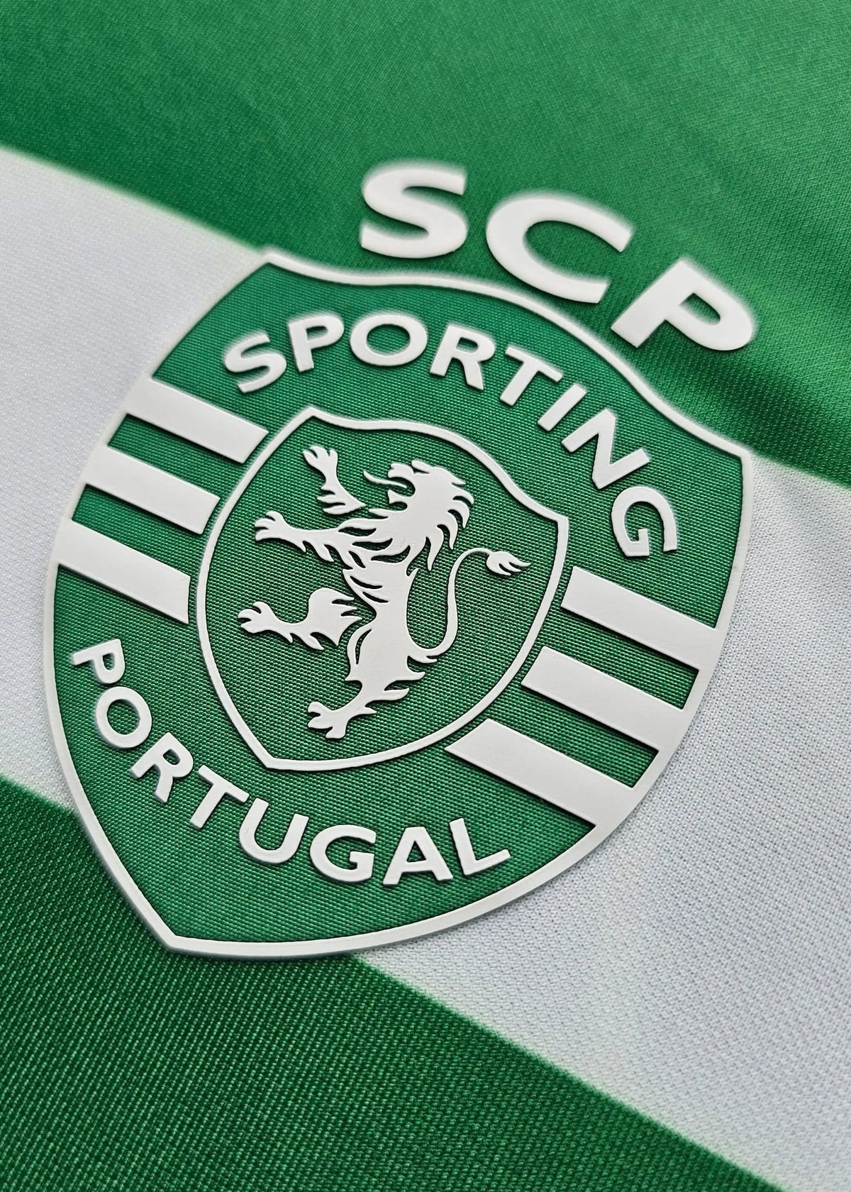Close-up of a Sporting Portugal soccer jersey with green and white horizontal stripes and the club crest featuring a silver lion.