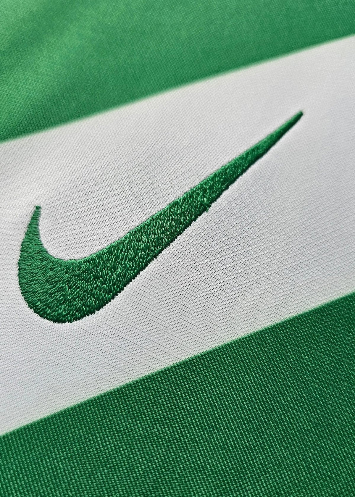 Close-up of the embroidered Nike swoosh on the green and white Sporting CP shirt fabric.