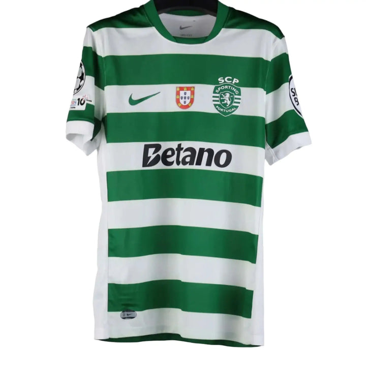 A green and white striped Sporting CP soccer jersey by Nike, hanging on a black hanger against a gray background. The jersey features the 'Betano' sponsor logo on the chest, the Sporting CP crest, and a Nike swoosh.