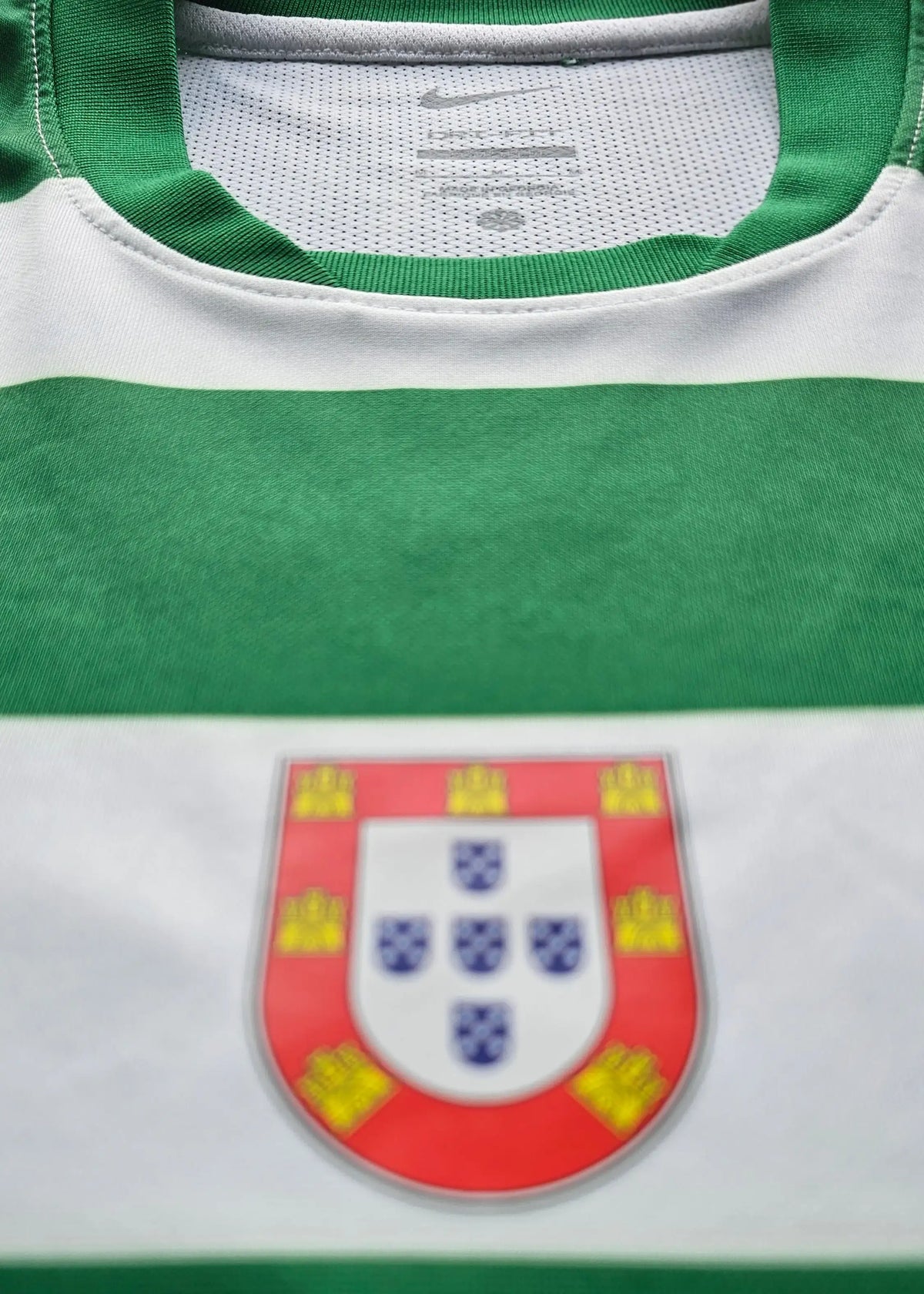 Close-up of a green and white striped soccer jersey with the Portugal national team crest on the chest. A white Nike brand tag is visible inside the collar.