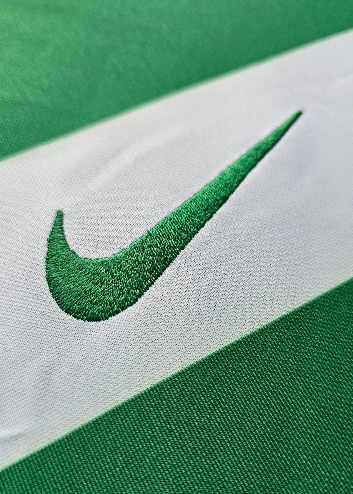 Close-up of the green Nike swoosh logo on green and white striped fabric, Flavio Gonçalves' Sporting CP shirt.