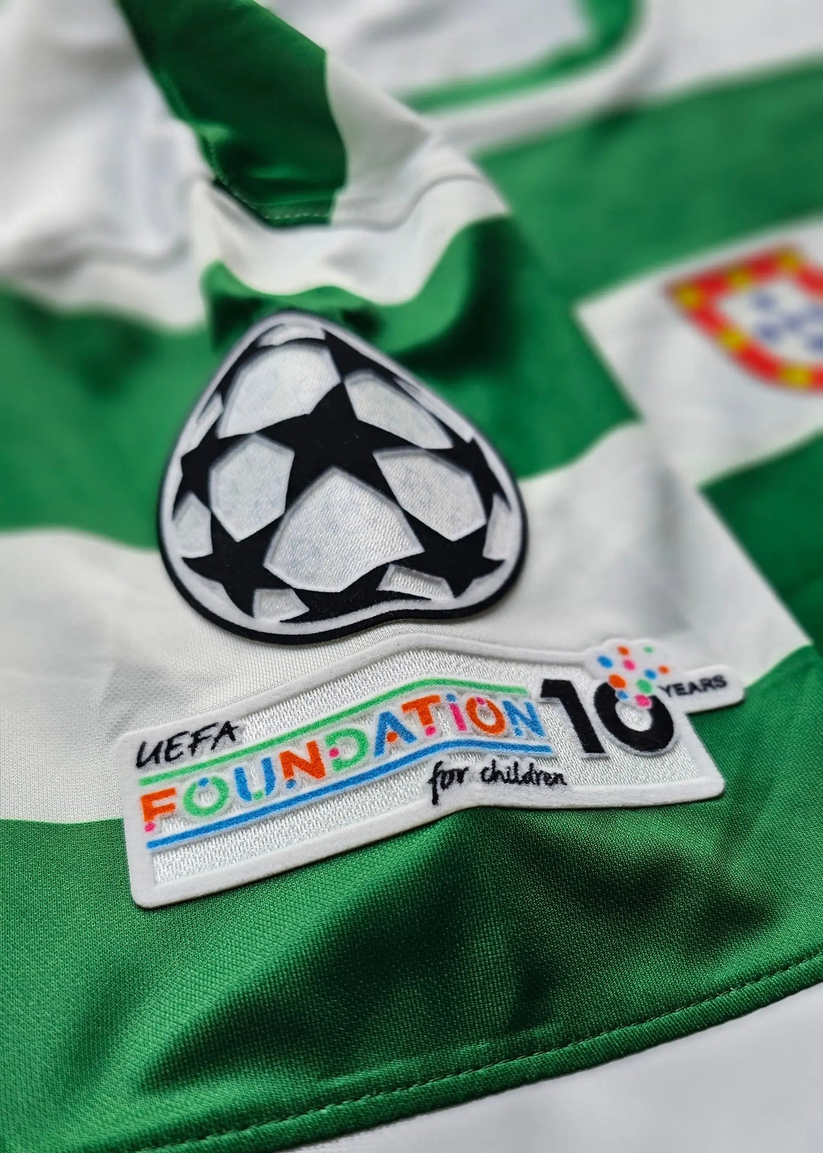 Close-up of the Champions League star-ball patch beside a UEFA Foundation 10 Years sleeve patch, Flavio Gonçalves' Sporting CP shirt.