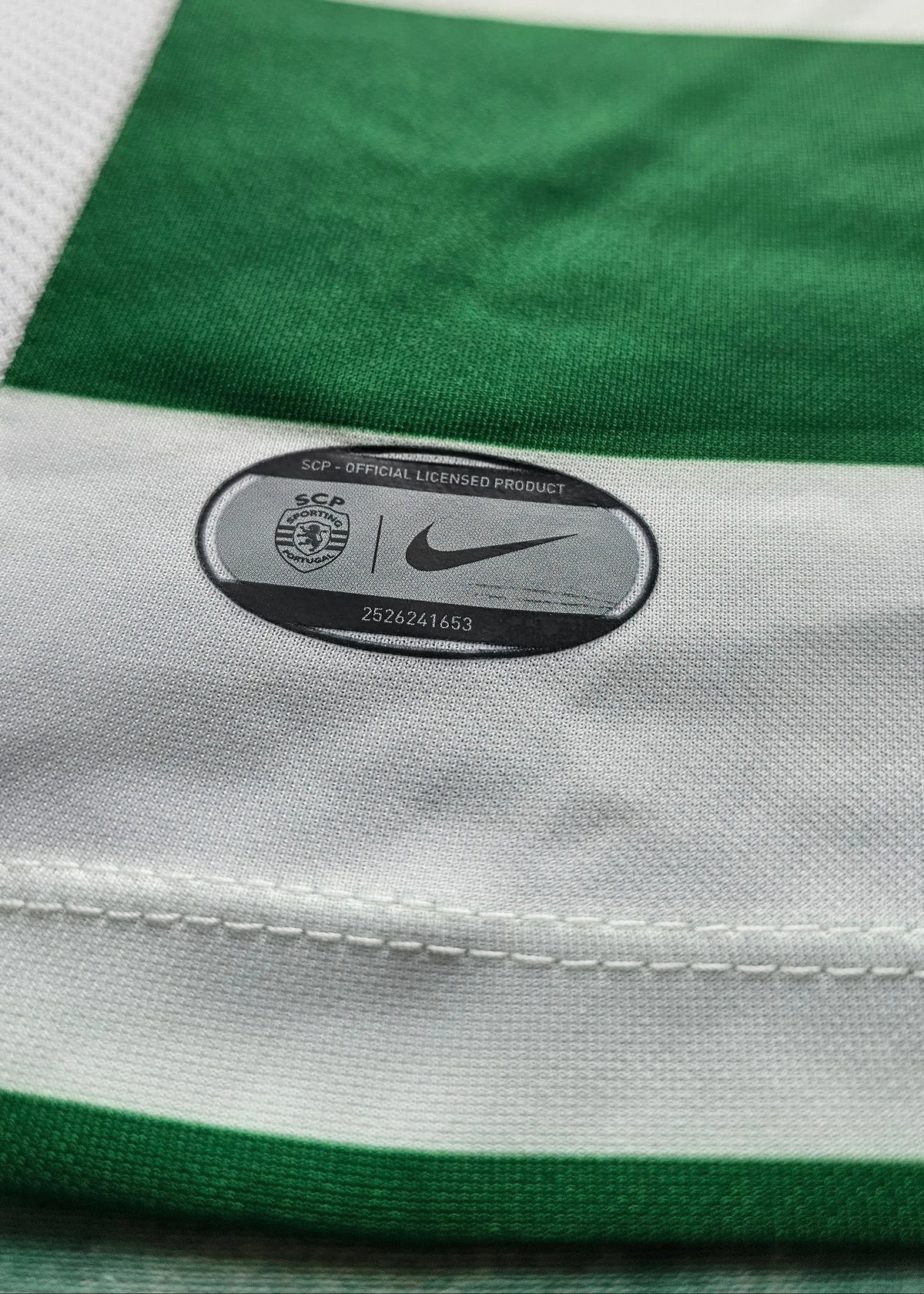 Close-up of a Nike and SCP official licensed product tag sewn into green and white striped fabric, Flavio Gonçalves' Sporting CP shirt.