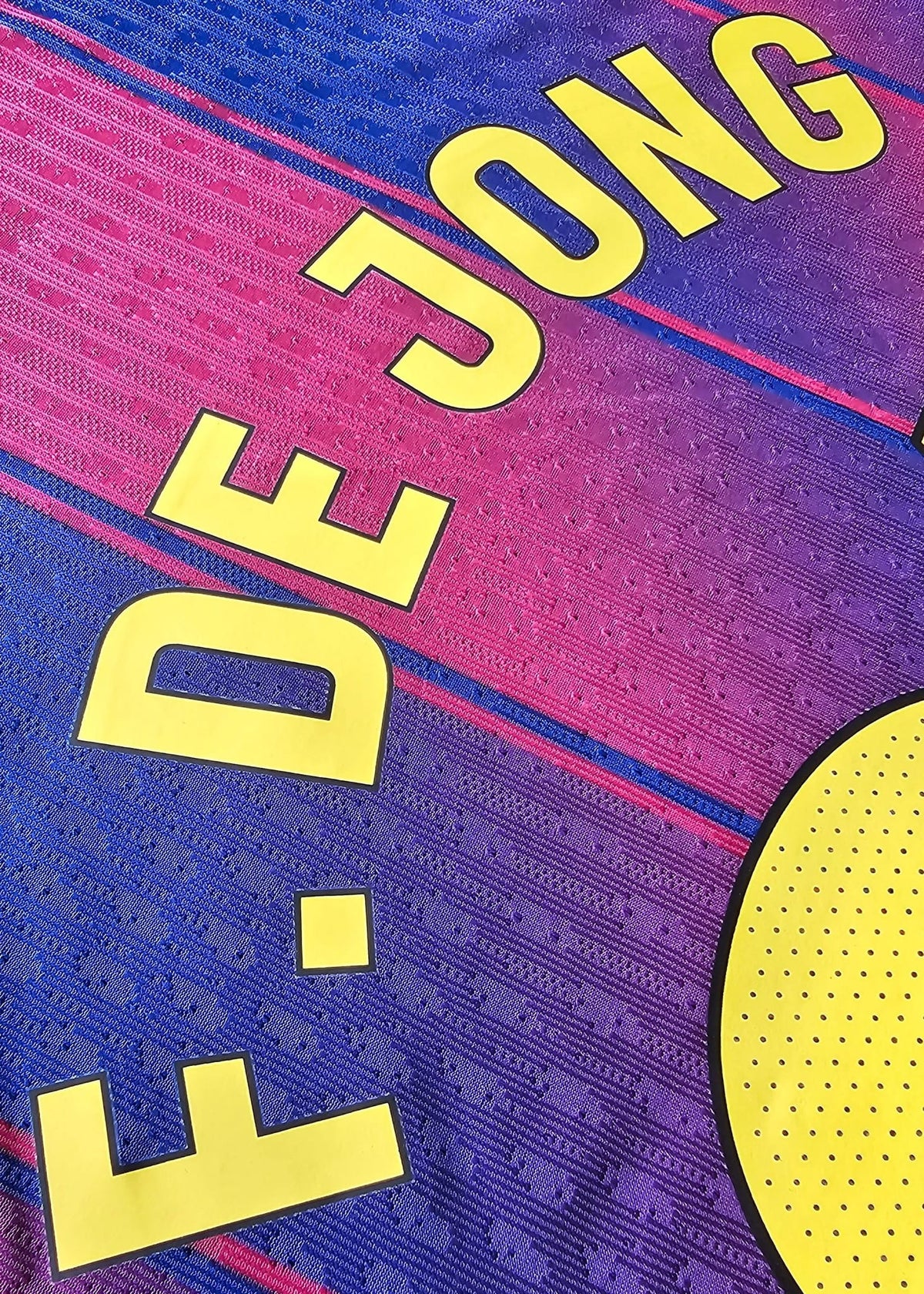 Close-up of a FC Barcelona soccer jersey showing the name 'F. DE JONG' in yellow lettering on the back, over a blue and red striped patterned fabric.
