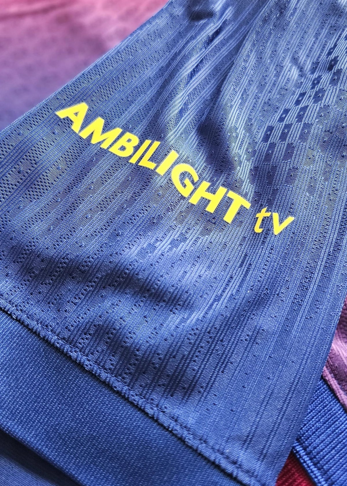 Yellow 'AMBILIGHT tv' sponsor wordmark printed on the blue fabric of Frenkie de Jong's FC Barcelona 2025-2026 shirt, No. 21.