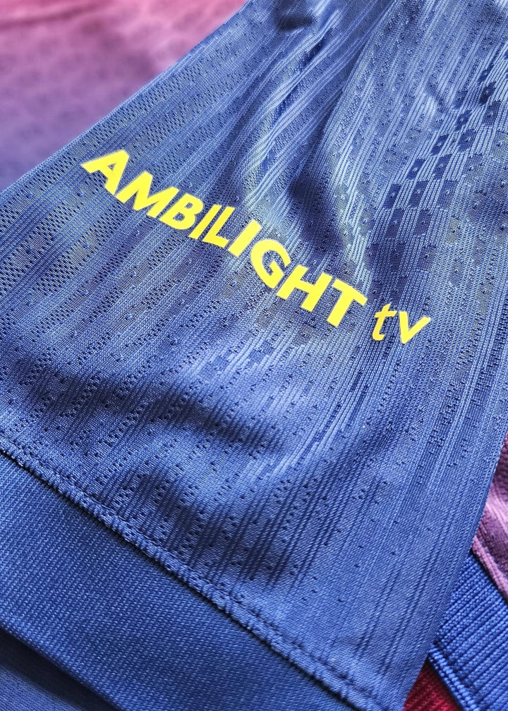 Yellow 'AMBILIGHT tv' sponsor wordmark printed on the blue fabric of Frenkie de Jong's FC Barcelona 2025-2026 shirt, No. 21.