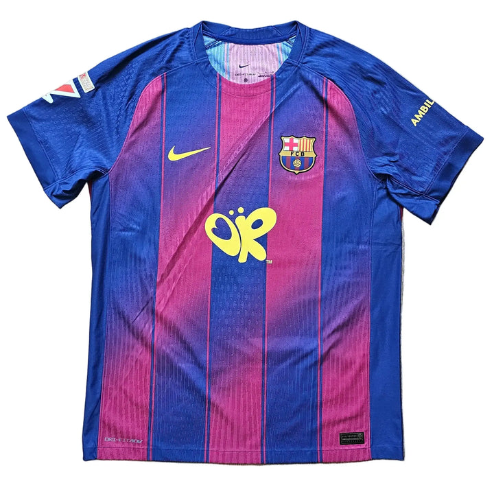 A Nike FC Barcelona home soccer jersey with blue and magenta vertical stripes. The jersey features the yellow FC Barcelona crest, a yellow Nike swoosh, and the yellow sponsor logo 'ÓR'.