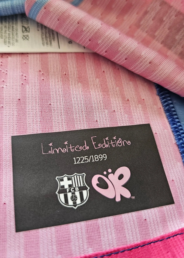 Black 'Limited Edition 1225/1899' tag with the FC Barcelona crest and pink Olivia Rodrigo butterfly logo, sewn into Frenkie de Jong's shirt.