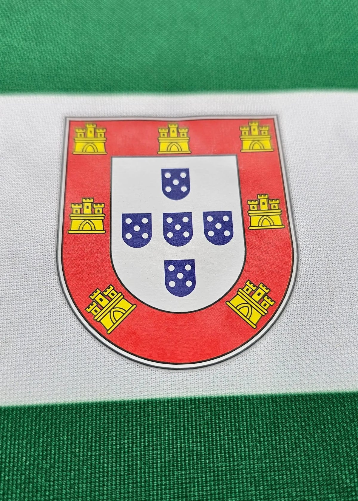 A close-up of a Portugal flag with a small metallic shield emblem featuring the Portuguese coat of arms in the center.