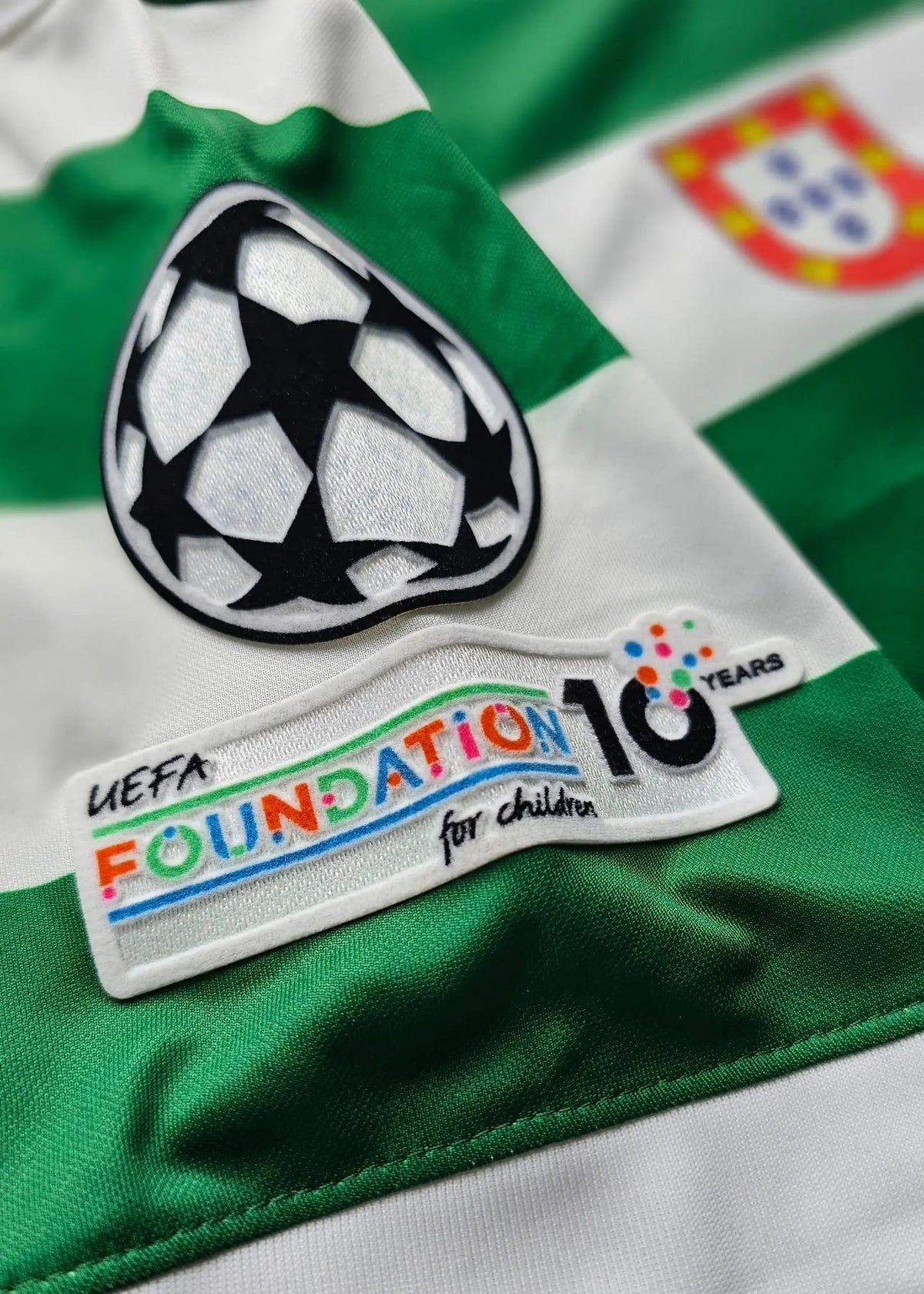 Close-up of a green and white striped soccer jersey with a UEFA Champions League patch and a UEFA Foundation 10 Years for Children patch on the chest.