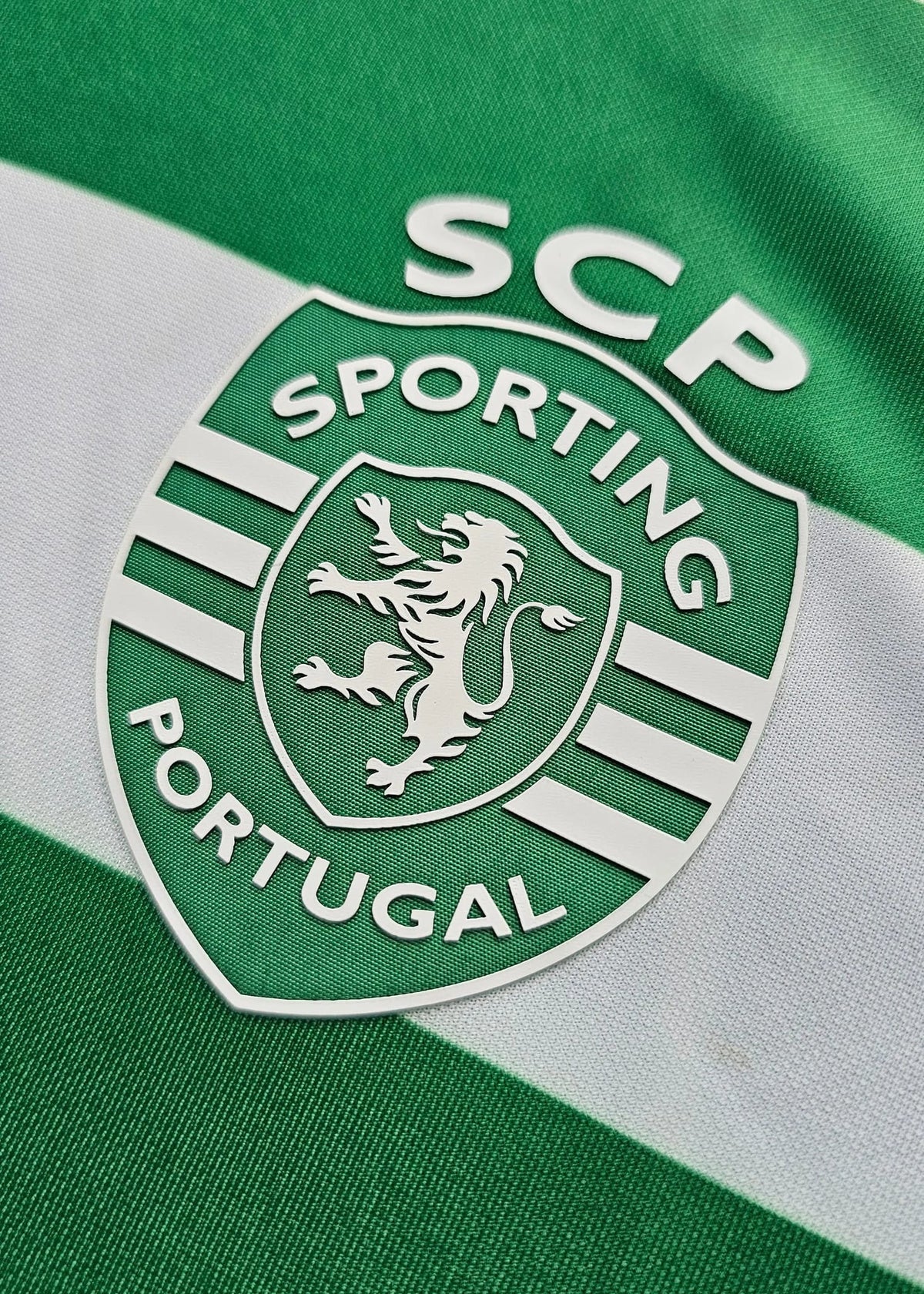 Close-up of a Sporting Portugal soccer jersey showing the green and white striped fabric with the club crest and 'SCP' text.