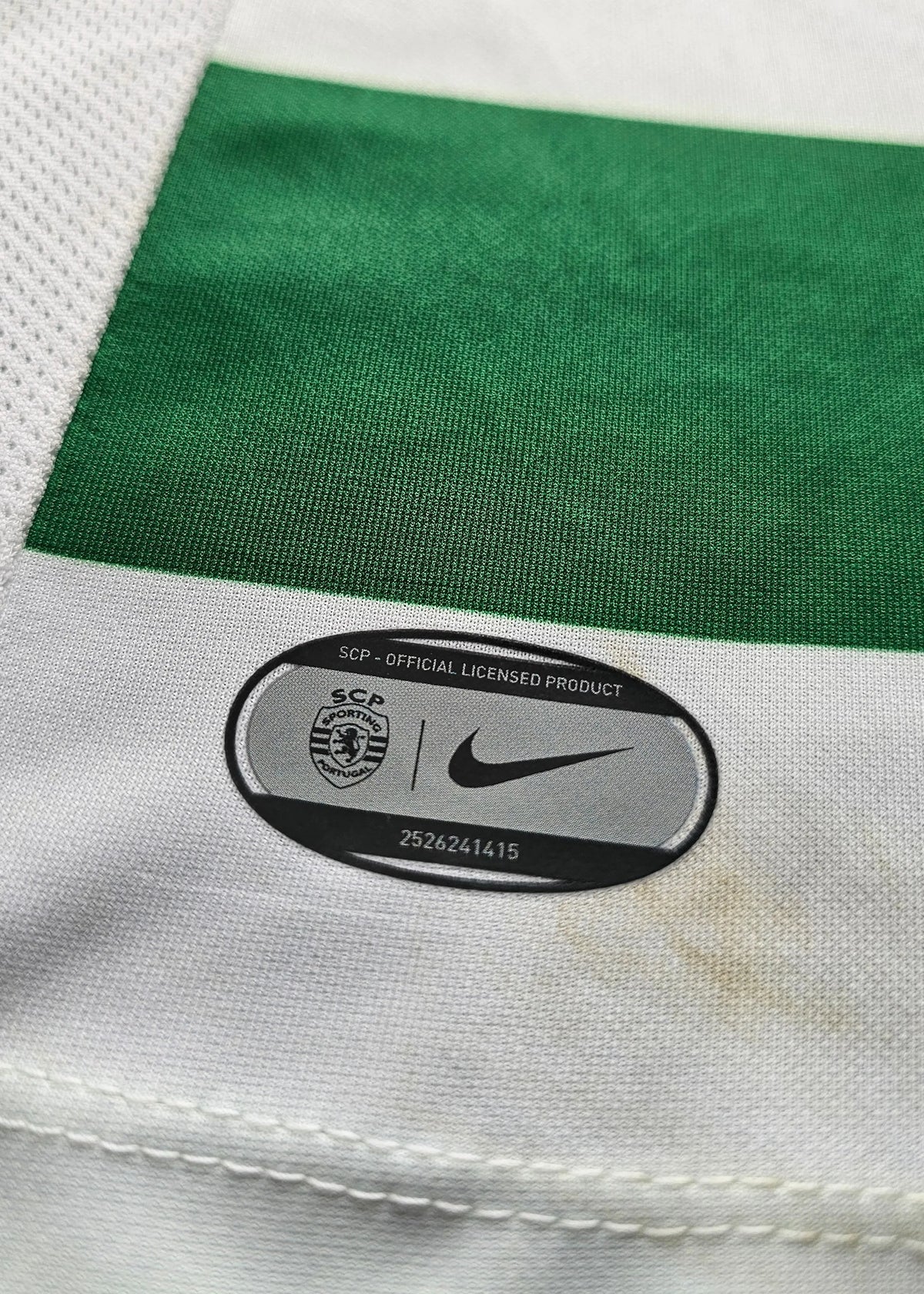 Close-up of a Nike and SCP official licensed product tag sewn into green and white striped fabric, Geovany Quenda Sporting CP shirt.