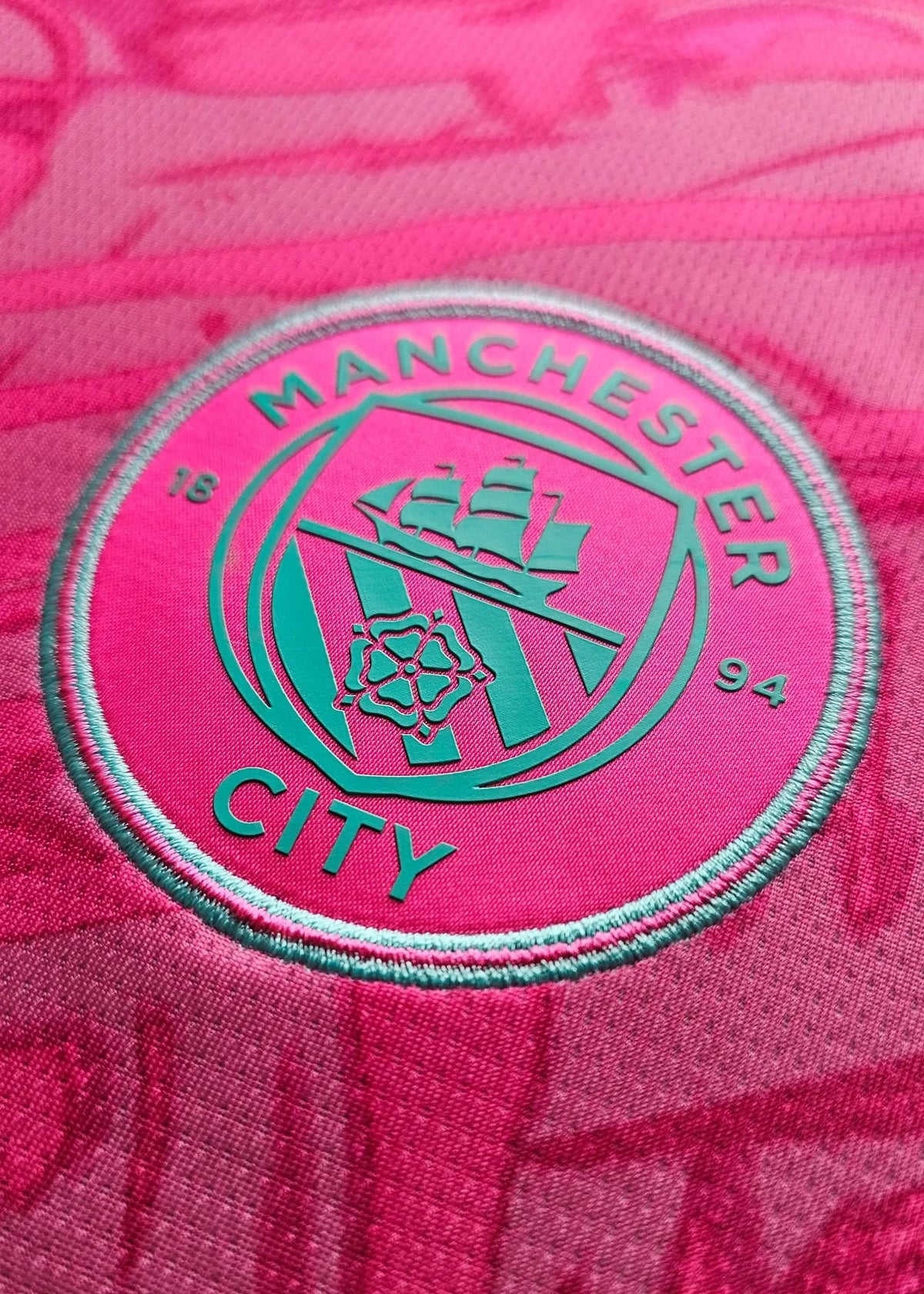 Back view displaying the Manchester City crest in teal on a pink background with the year 1894.