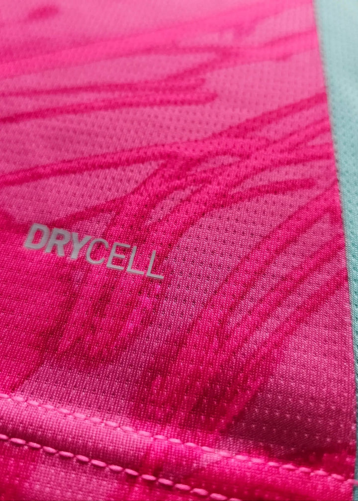 Close-up of the pink fabric showing white 'DRYCELL' text beside the teal side panel of a Manchester City goalkeeper shirt.