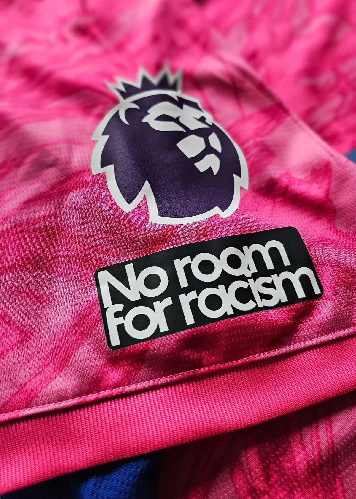 Close-up showing the Premier League lion crest and 'No room for racism' on a pink football shirt.