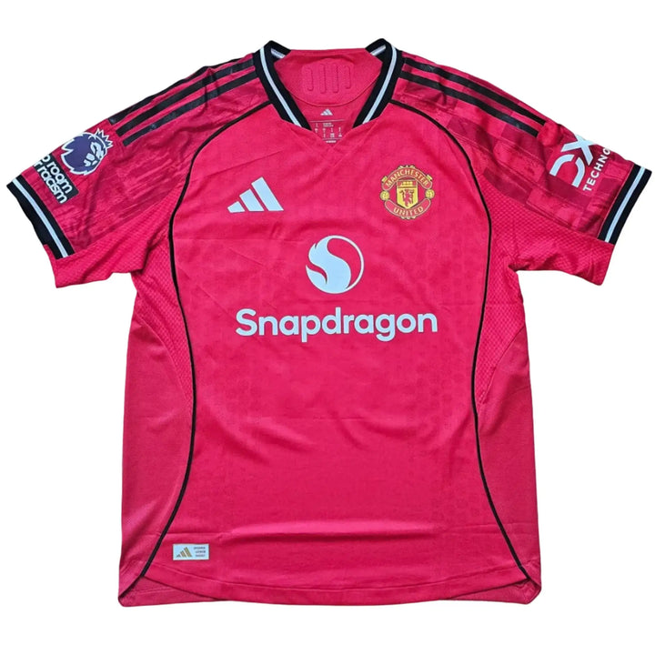 Front of a pink Manchester United shirt laid flat, adidas logo and club crest above the Snapdragon sponsor text and a 'No Room For Racism' sleeve patch.