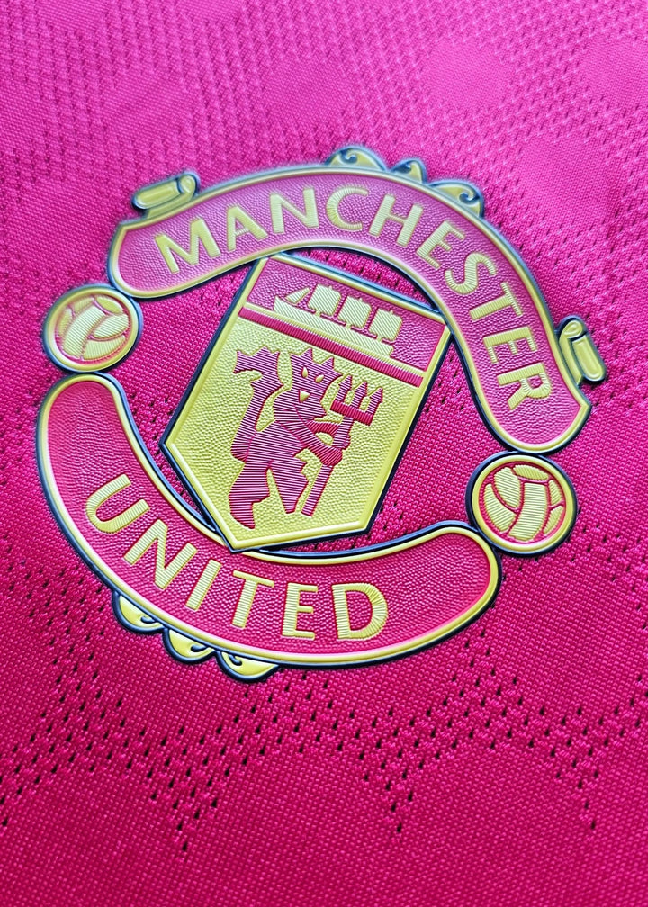 Close-up of Manchester United crest in yellow on red background with football detail.