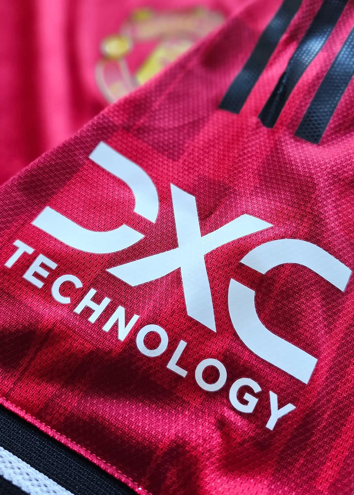 Close-up view of the DXC Technology sponsor logo on a red Manchester United football shirt.