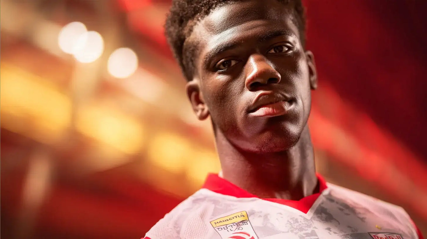 Joane Gadou in Red Bull Salzburg white football shirt with red collar and subtle grey pattern, standing under warm stadium lights.