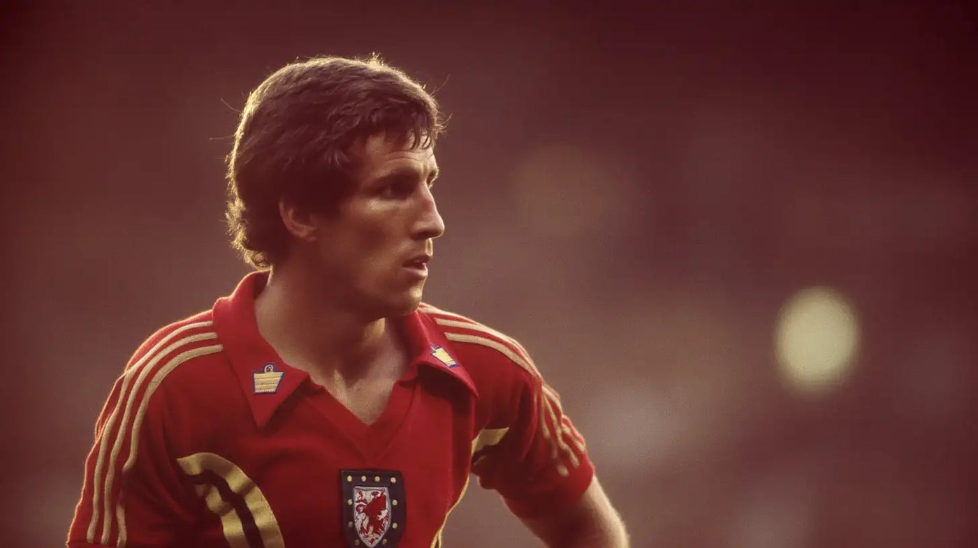 Joey Jones in a red Wrexham football shirt with gold trim and club crest, captured in action with stadium lights glowing in the background.