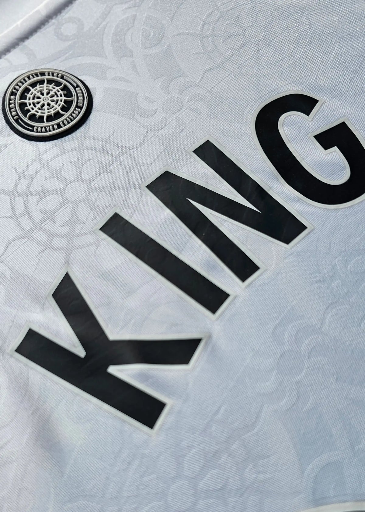 Close-up of the black KING nameset lettering beside the Fulham FC Craven Cottage crest patch, Josh King's Fulham F.C. 2025-2026 shirt.