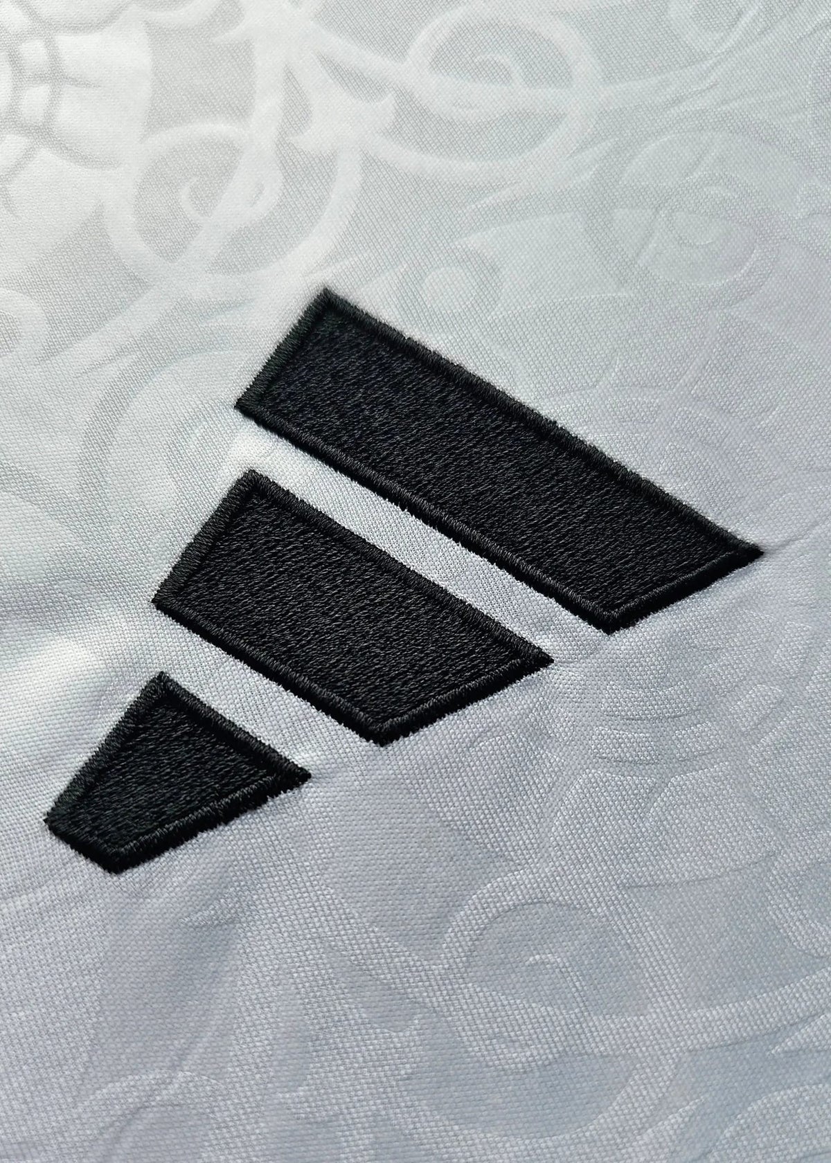 Close-up of the black Adidas three-stripe logo on the sleeve of white fabric, Josh King's Fulham F.C. 2025-2026 shirt.