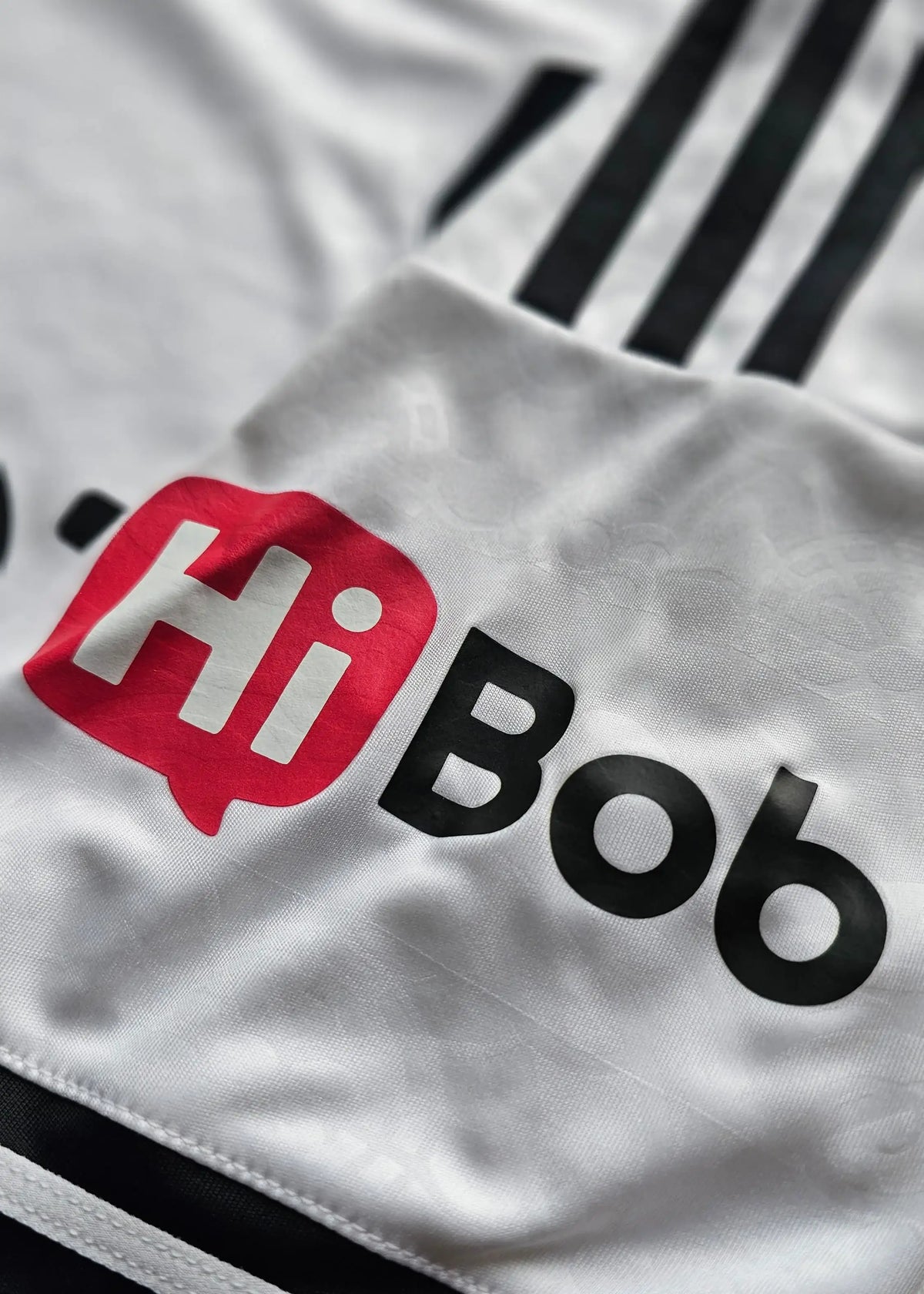 Close-up of a white athletic jersey with black stripes and a large red and black 'HiBob' sponsor logo printed on the chest.