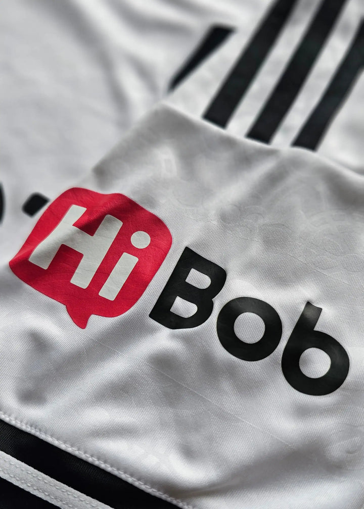 Close-up of a white athletic jersey with black stripes and a large red and black 'HiBob' sponsor logo printed on the chest.