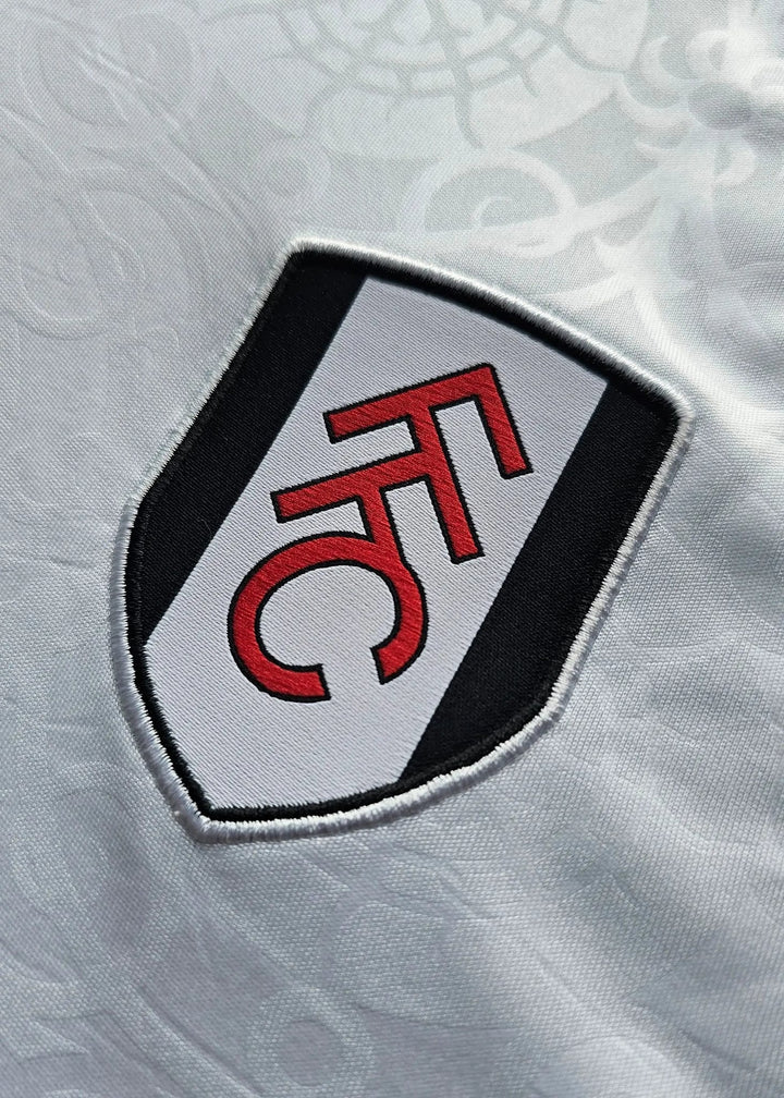 Close-up of the red and black Fulham FC shield crest embroidered on white fabric, Josh King's Fulham F.C. 2025-2026 shirt.