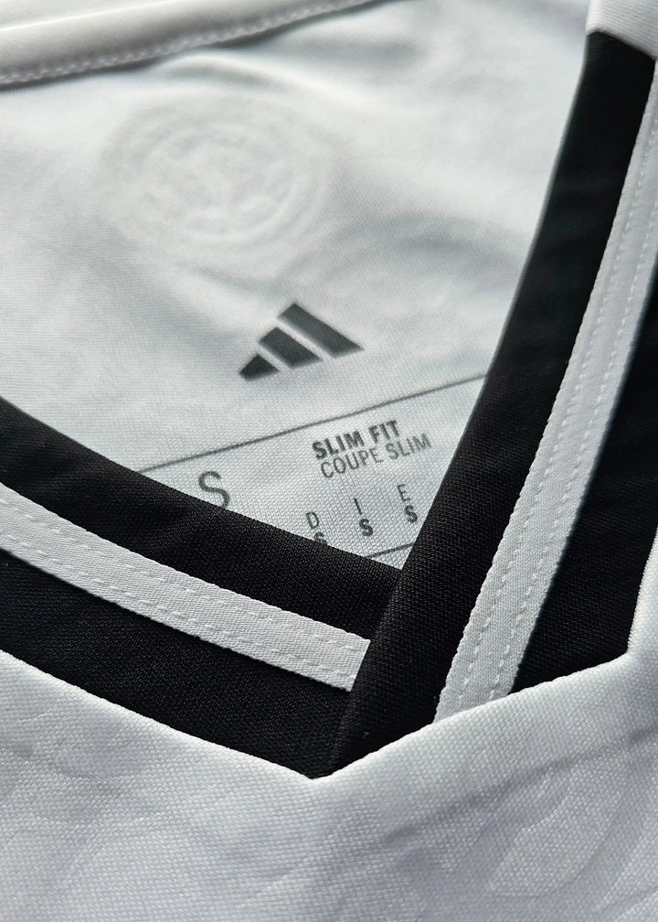 Close-up of a white Adidas soccer jersey with black trim along the V-neck collar, showing the inner neck label with size information.